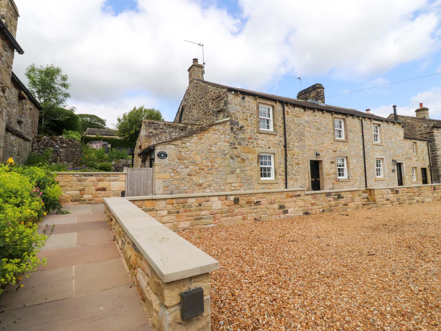 A stone house with a gravel driveway and pathway at Rose Tree Cottage in Skipton