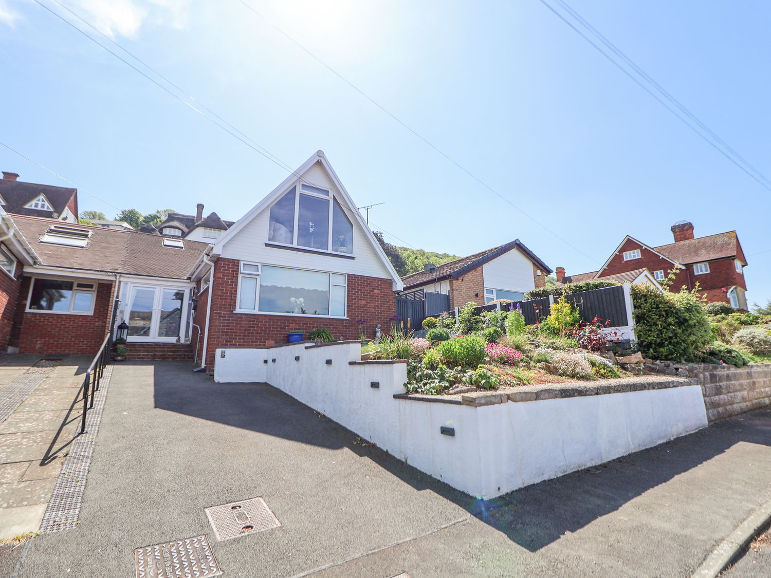 A brick house with a large window and sloped roof next to a garden and driveway at 67 Pendre Avenue in Prestatyn