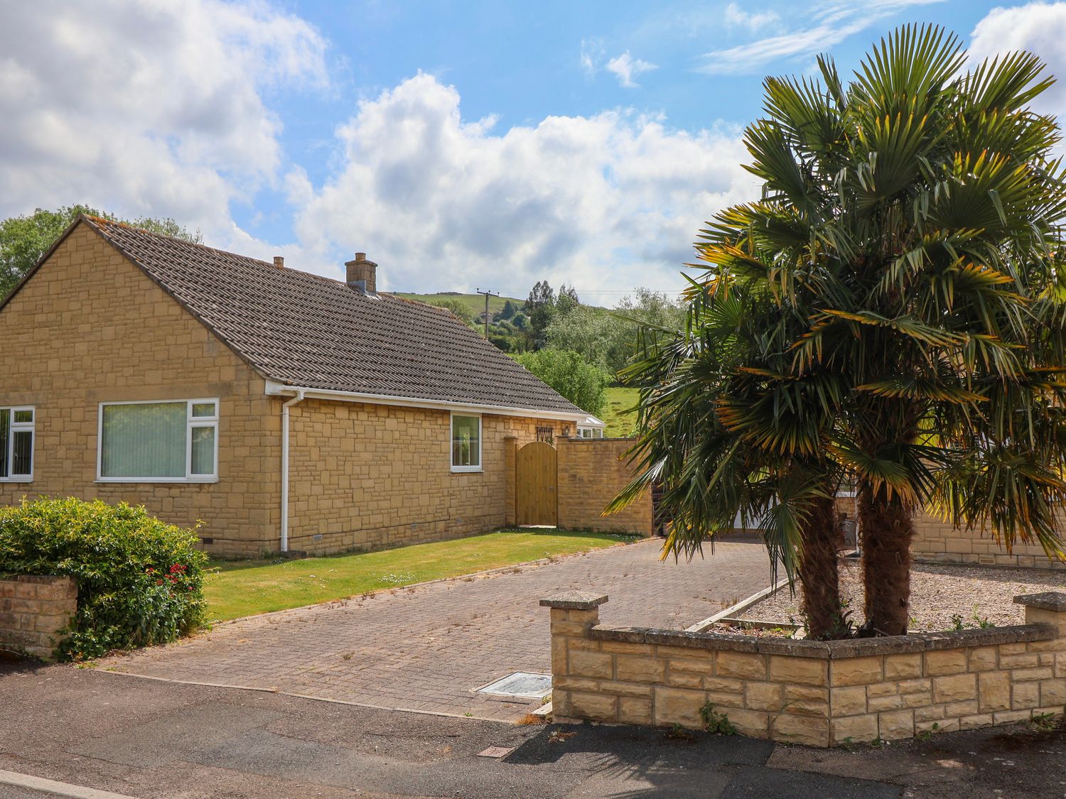 A single-story house with a tiled roof next to a driveway and palm trees at Hillside in Bishops Cleeve