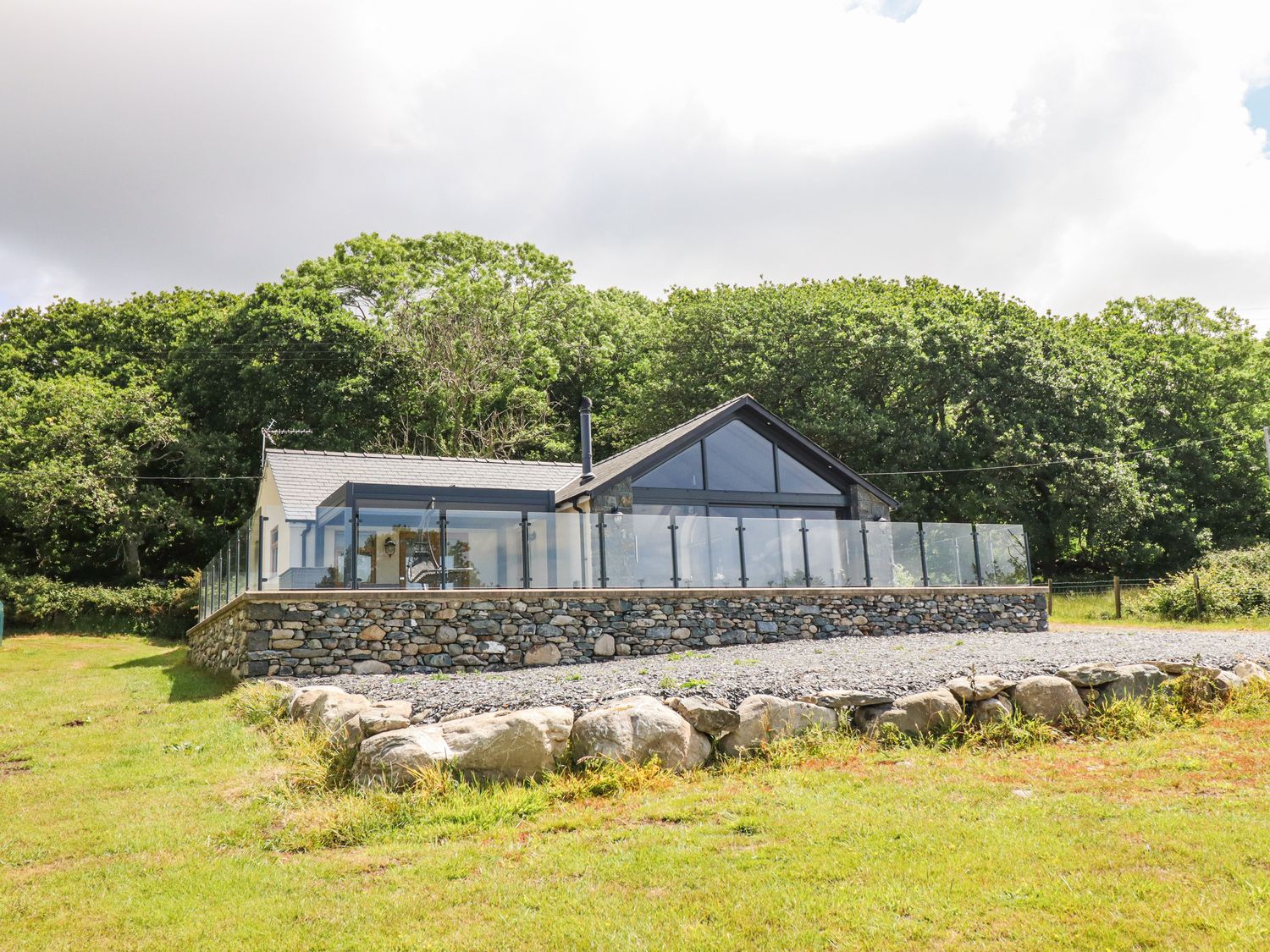 A house with a glass railing and stone wall in a garden at Perth Y Deri in Llanddwywe