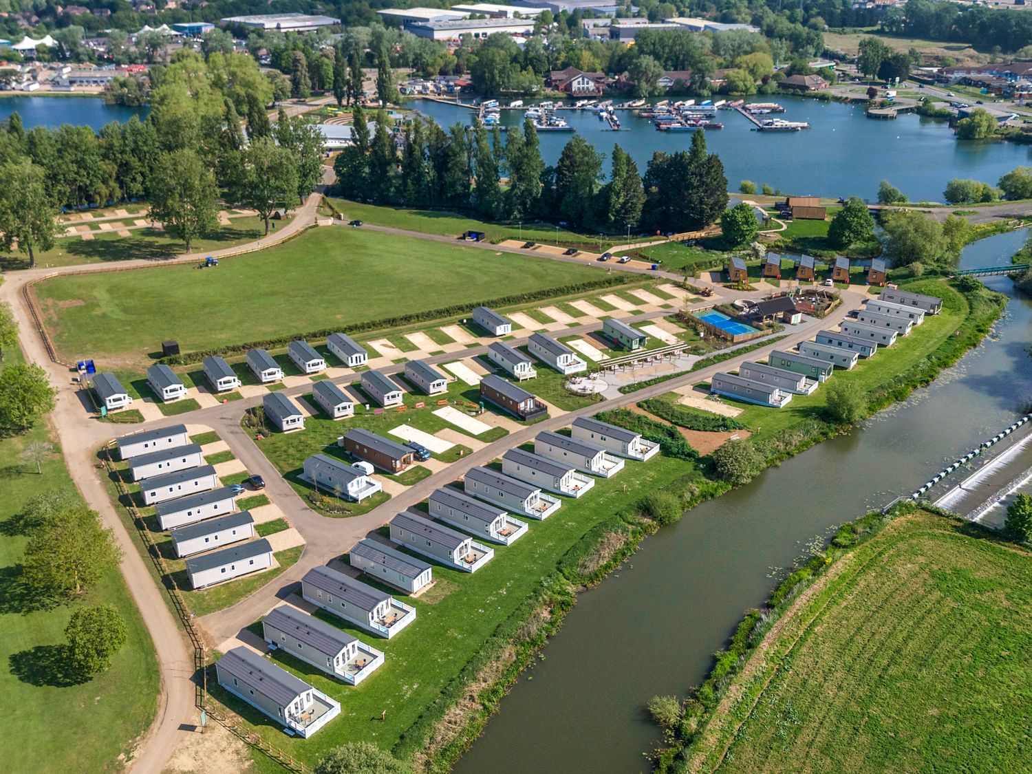 An aerial view of a holiday park with multiple caravans arranged in rows near a river and a lake at Brookside Bliss - Billing Aquadrome in Billing Aquadrome Holiday Park