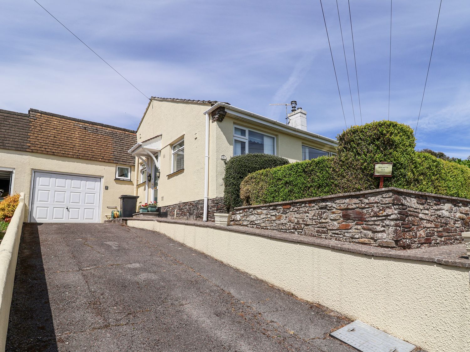 A driveway leading to a house with a garage and stone wall with shrubs at Ambermist in Churchstow