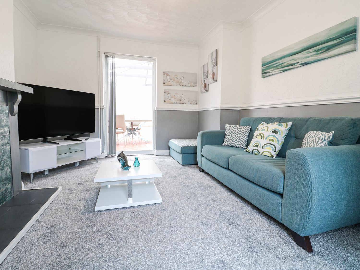 A living room with a teal sofa a white coffee table a large flat-screen TV and grey carpet at 46 Dalby Road in Antsey