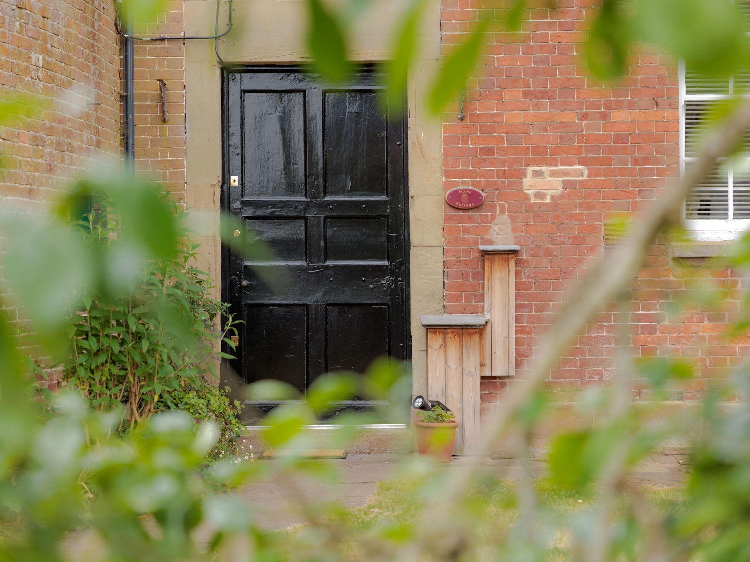 A black door with a plaque and a plant pot at Game Cottage in Bridgnorth