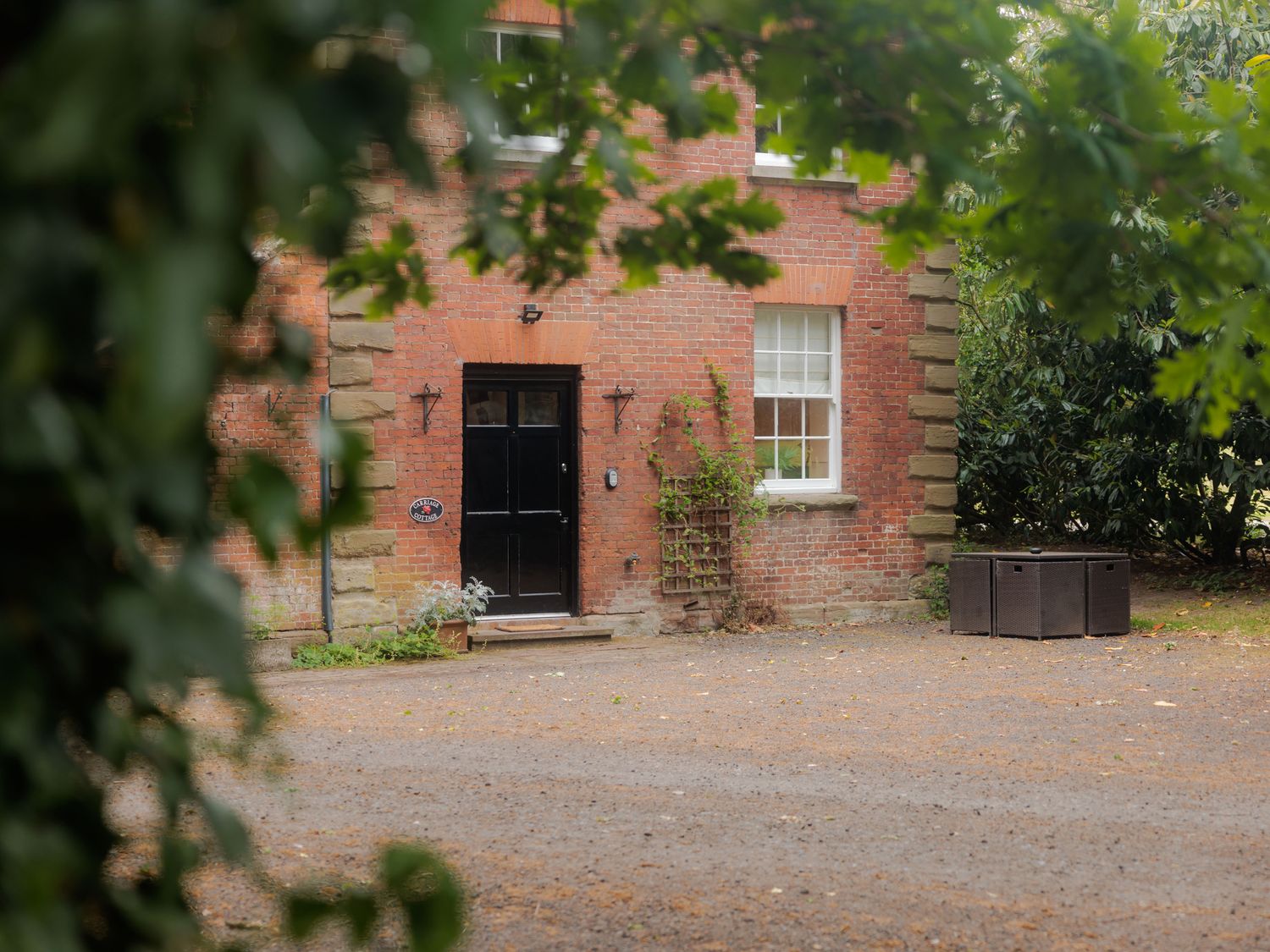 An exterior view of a red brick house with a black door and windows at Carriage Cottage in Worfield near Bridgnorth