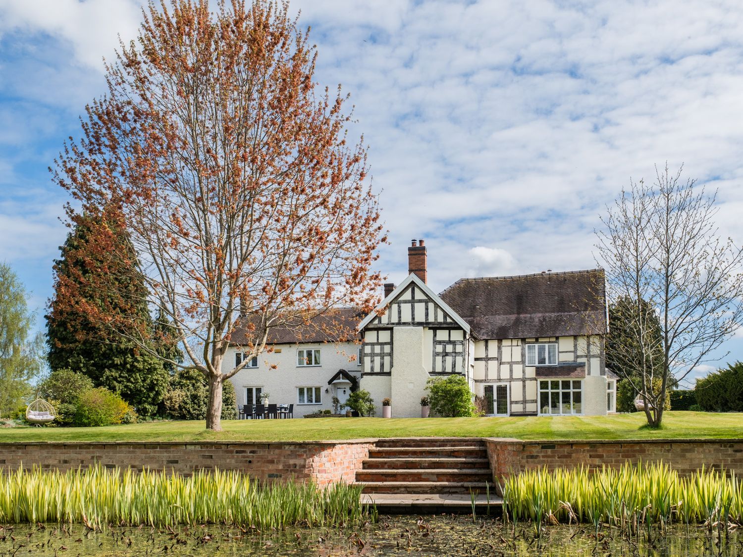 A house surrounded by a garden with trees and a water feature at Hall O'Coole in Broomhall nearn Wrenbury