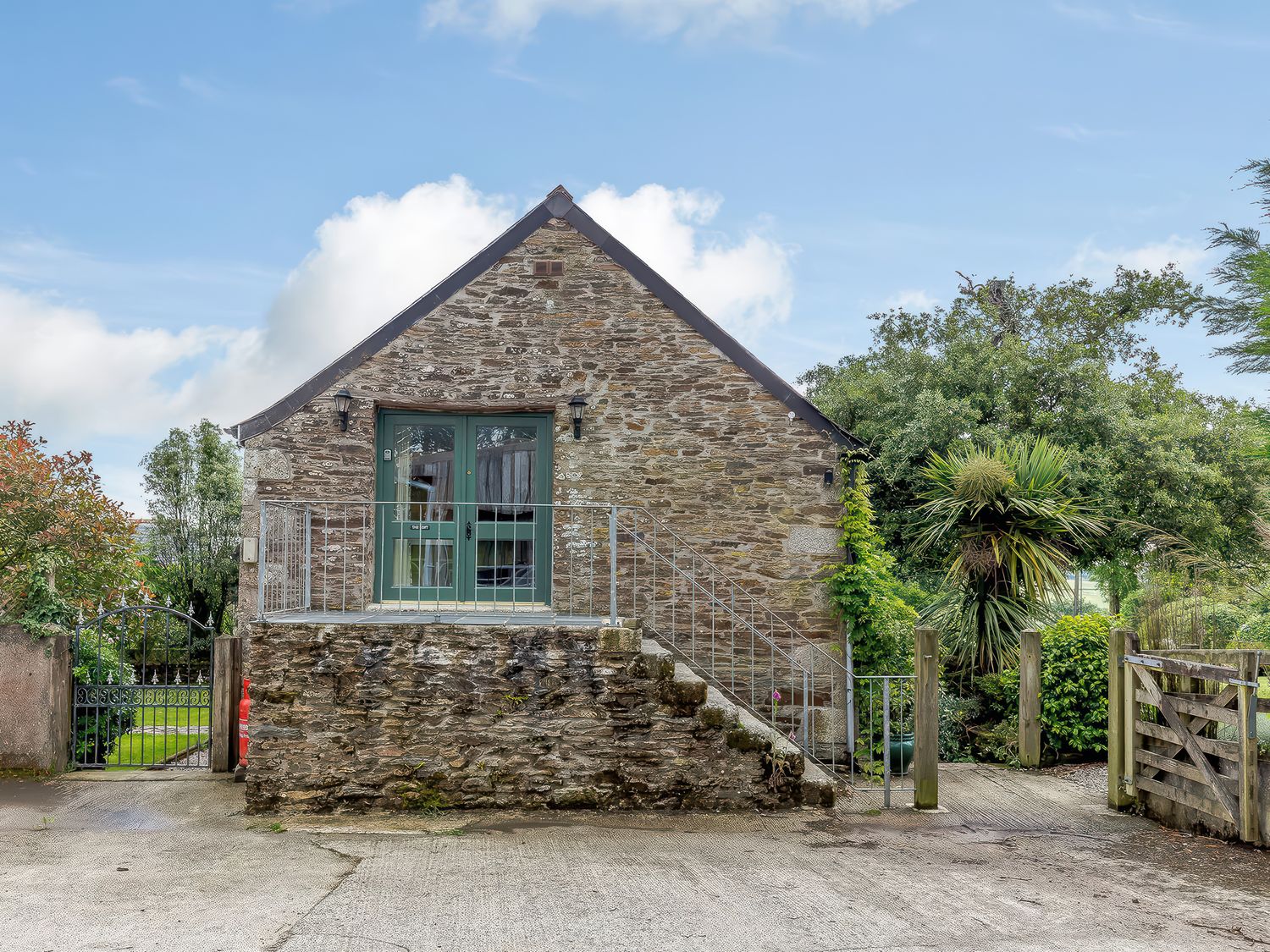 A stone building with a green door at the top of stairs surrounded by plants at The Loft in Bodrean near Truro