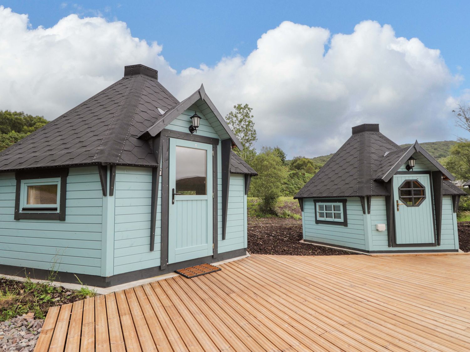 Two blue wooden huts with black roofs on a wooden deck at Little Luxe Lodges Balmacara near Kyle of Lochalsh