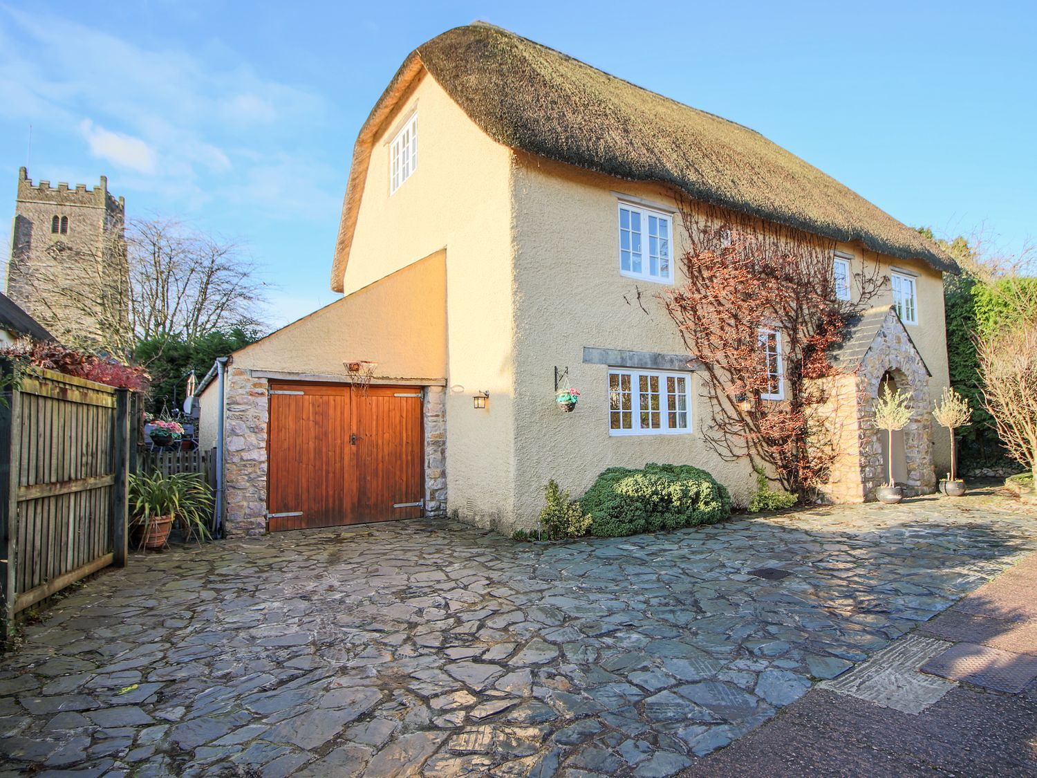 A house with a thatched roof stone driveway and garage near a church at Church Thatch in Abbotskerswell