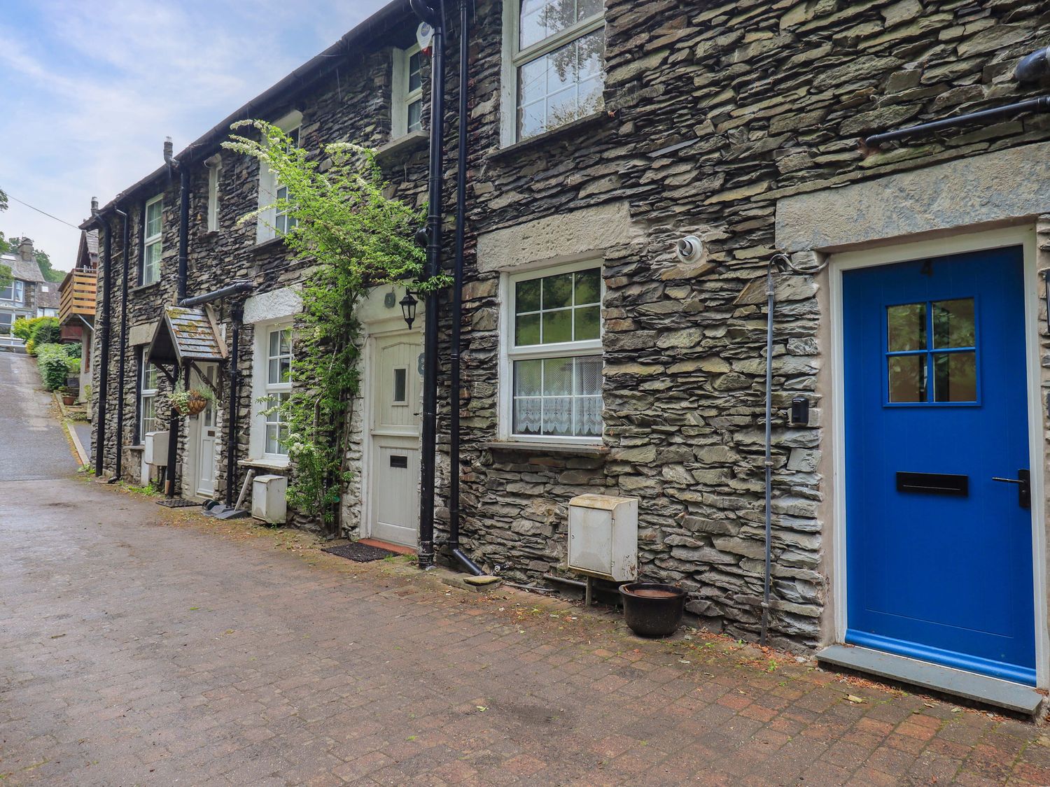 A stone building with a blue door and plants at Stoker’s Cottage Windermere