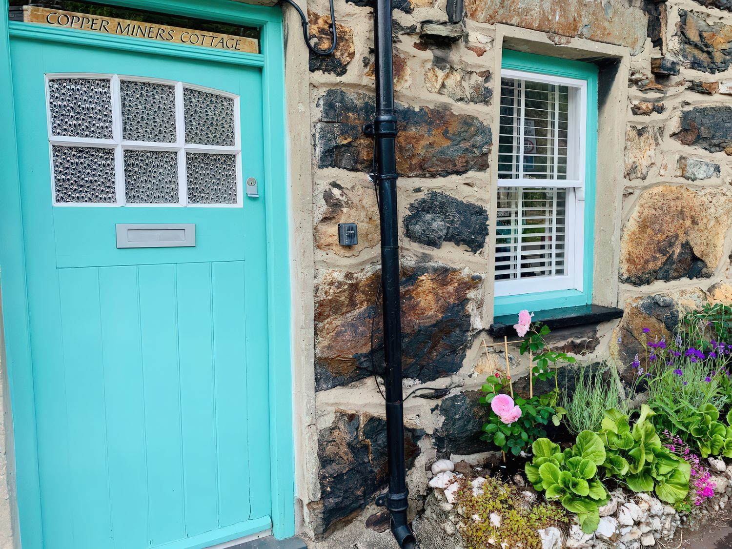 A door and window with a flowerbed at Copper Miners Cottage in Beddgelert, Eryri (snowdonia)