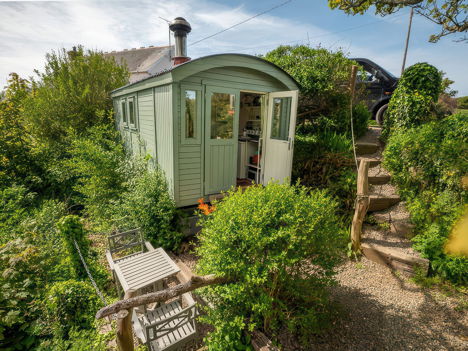 A hut surrounded by greenery with steps leading to a driveway at The Shepherd Hut near Nine Wells near Solva