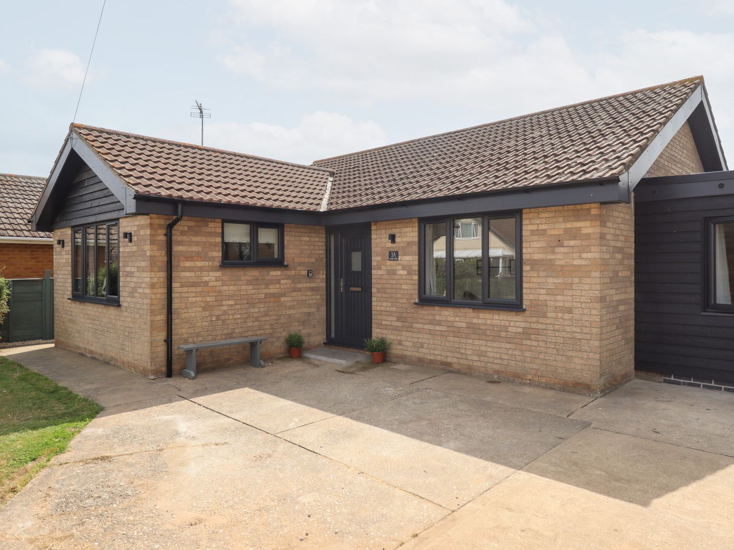 A front view of a bungalow with a pathway and plants at Sandy Toes in Trusthorpe