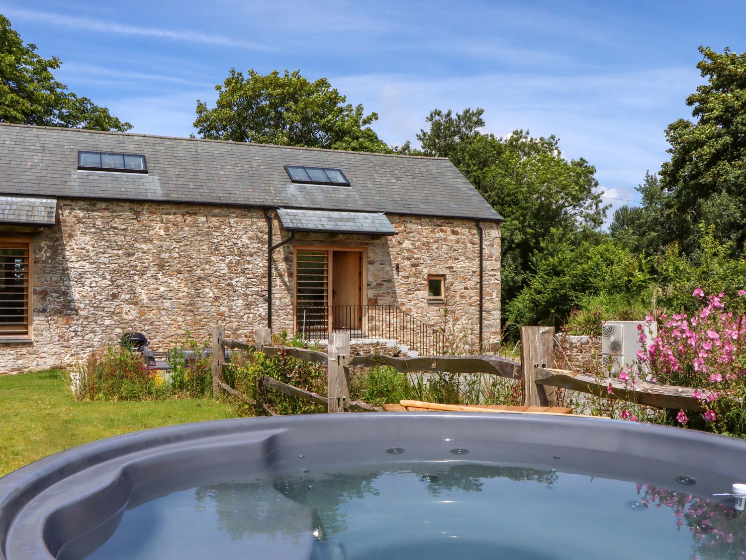 An outdoor area with a hot tub and a stone building at Lower Walreddon Barn in Tavistock