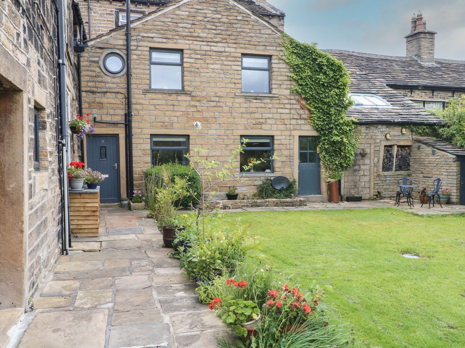 A garden area with a building and plants at Cottage Round T'Corner Holmfirth