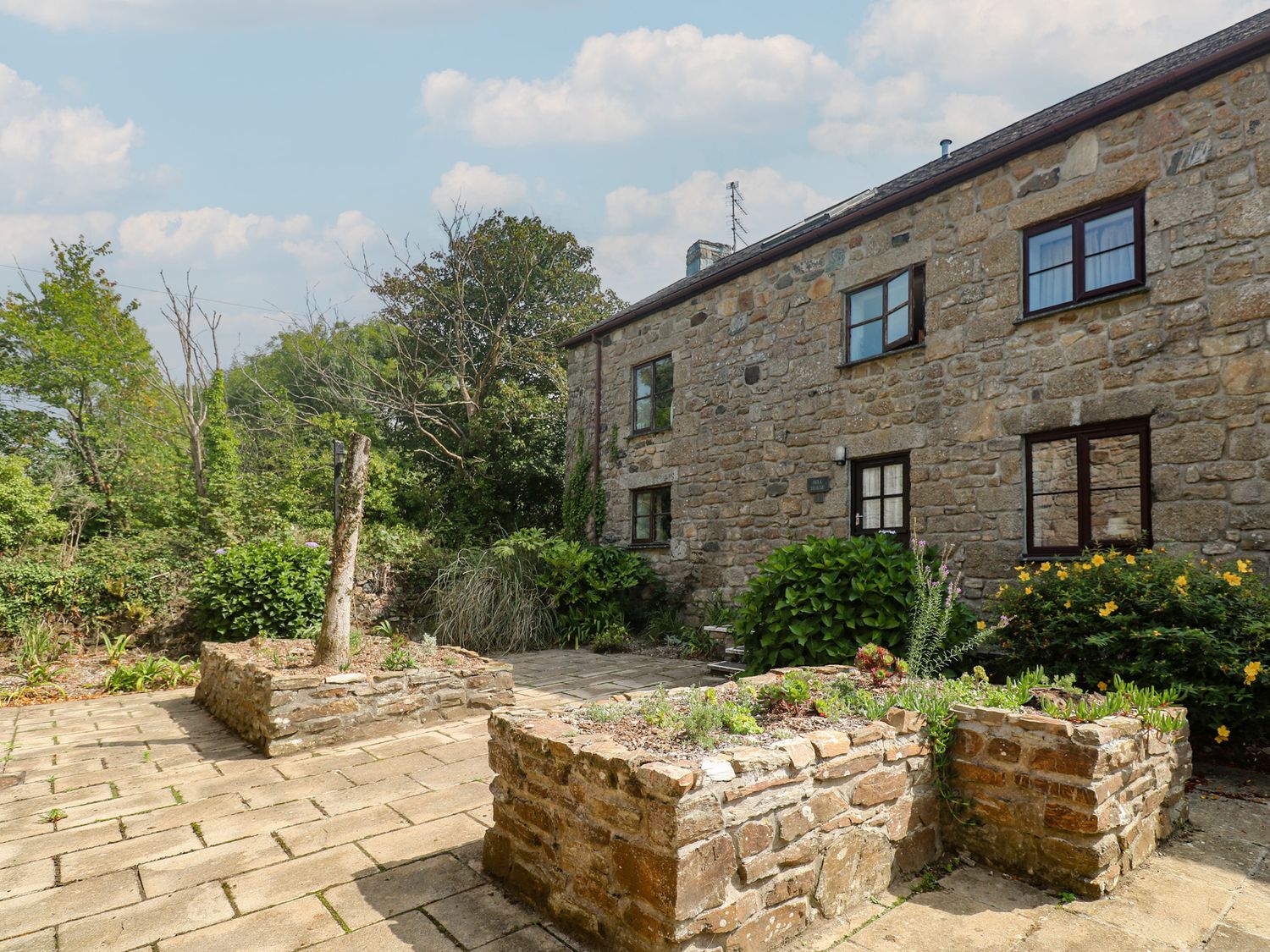 A stone house with a patio and plants at Mill House Barn in Gulval near Penzance