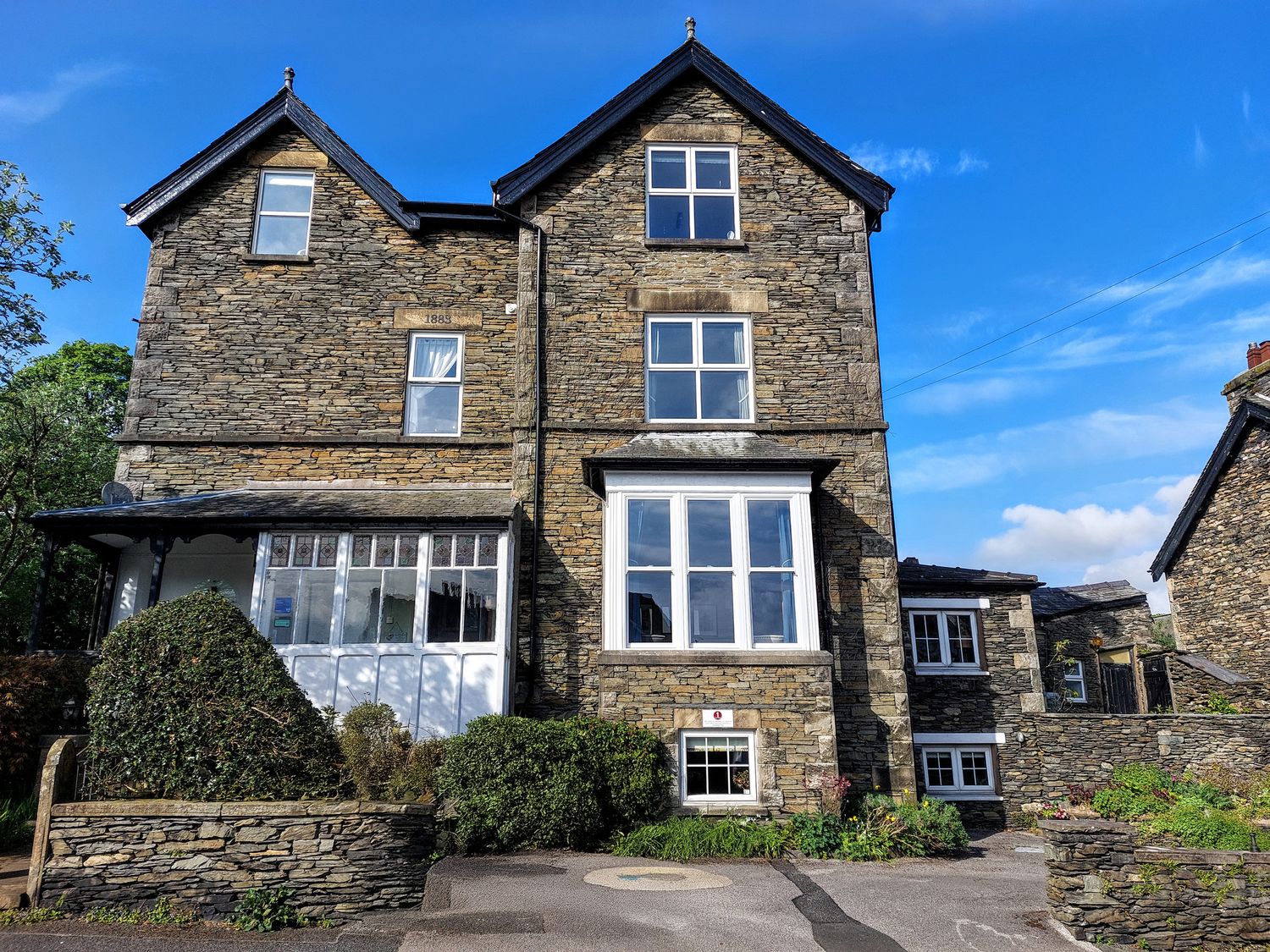An exterior view of a stone building with windows and bushes at 1 Park Road Windermere