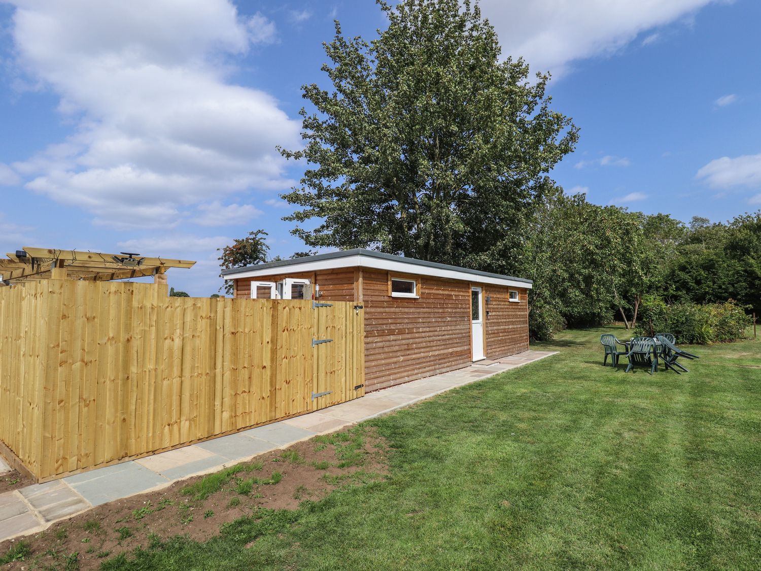 A shed with a fence and seating in a garden at Pear Tree Lodge in Alford