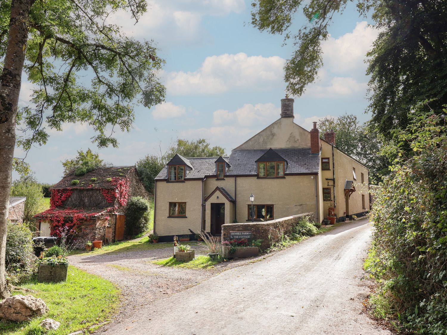 A cottage with a driveway and trees at Denhill Cottage in Chipstable near Wiveliscombe