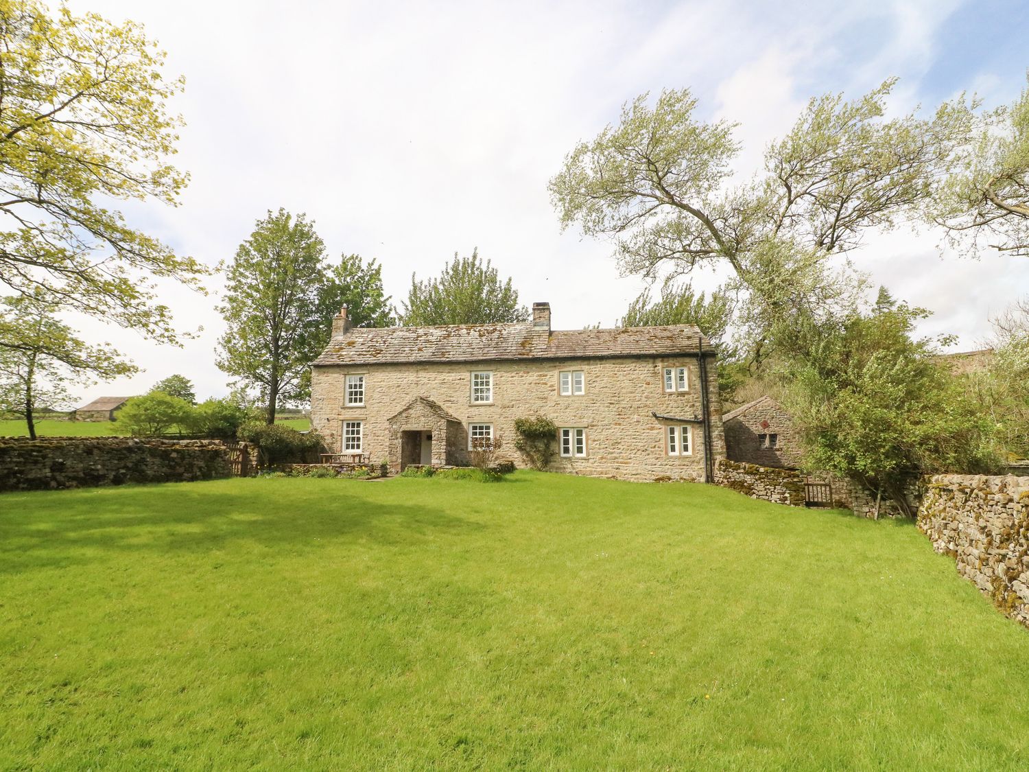 A stone house with a lawn and trees surrounded by stone walls at Cowstonegill in West Burton