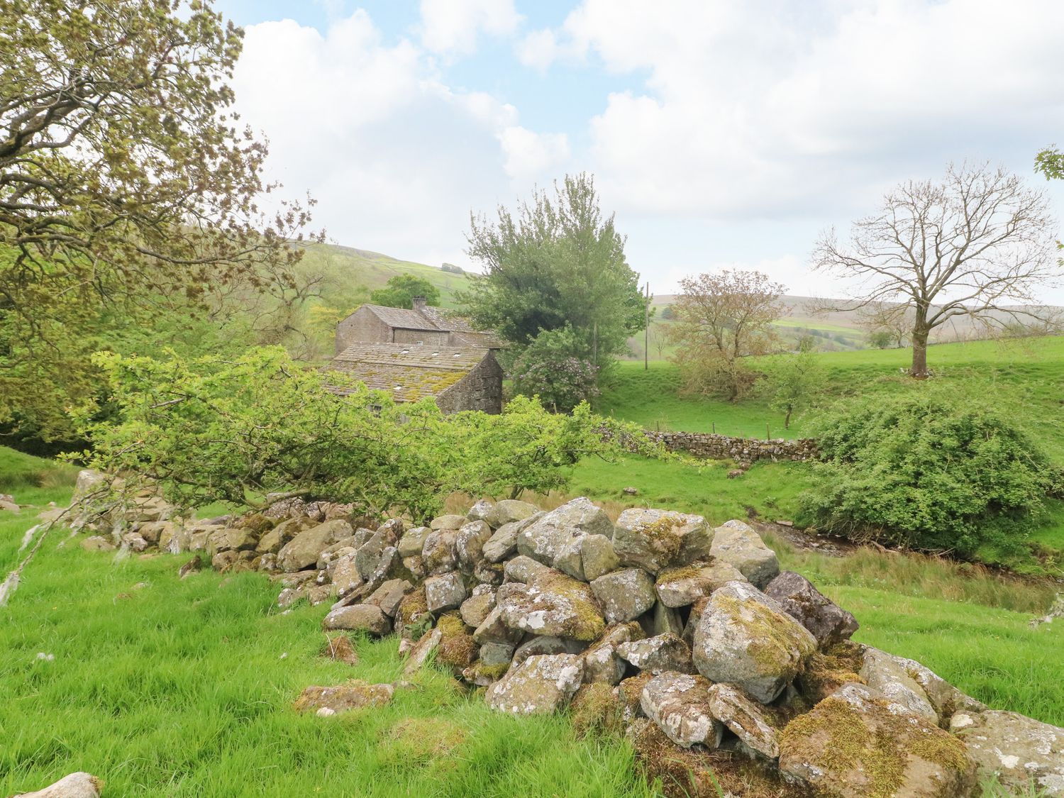 A stone wall and trees with a stone building in the background at Cowstonegill in West Burton