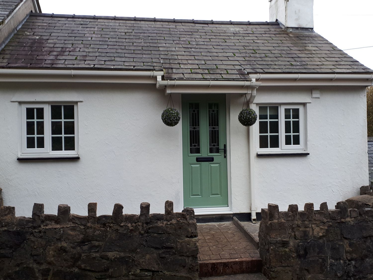 A house with a green door and windows at Bryn Bach in Pentraeth