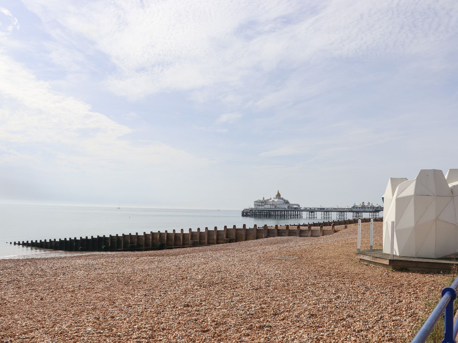 View of a pier and beach with a geometric cabin at Pebbles Eastbourne