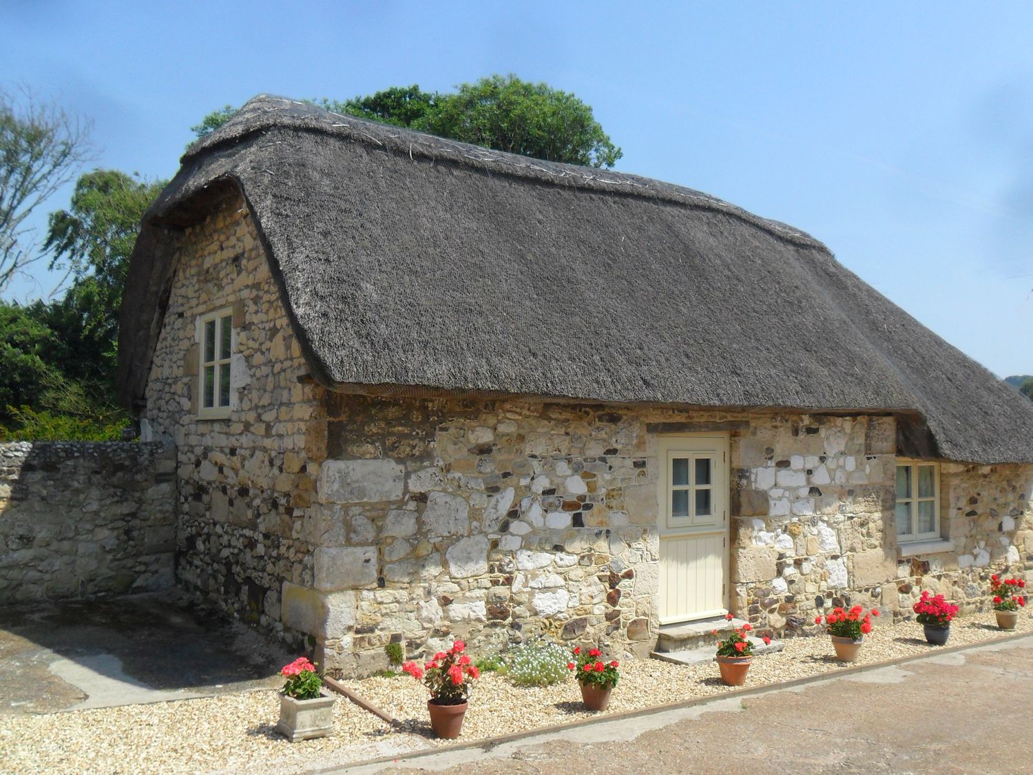 A stone cottage with a thatched roof and flower pots at Sheepwash Barn