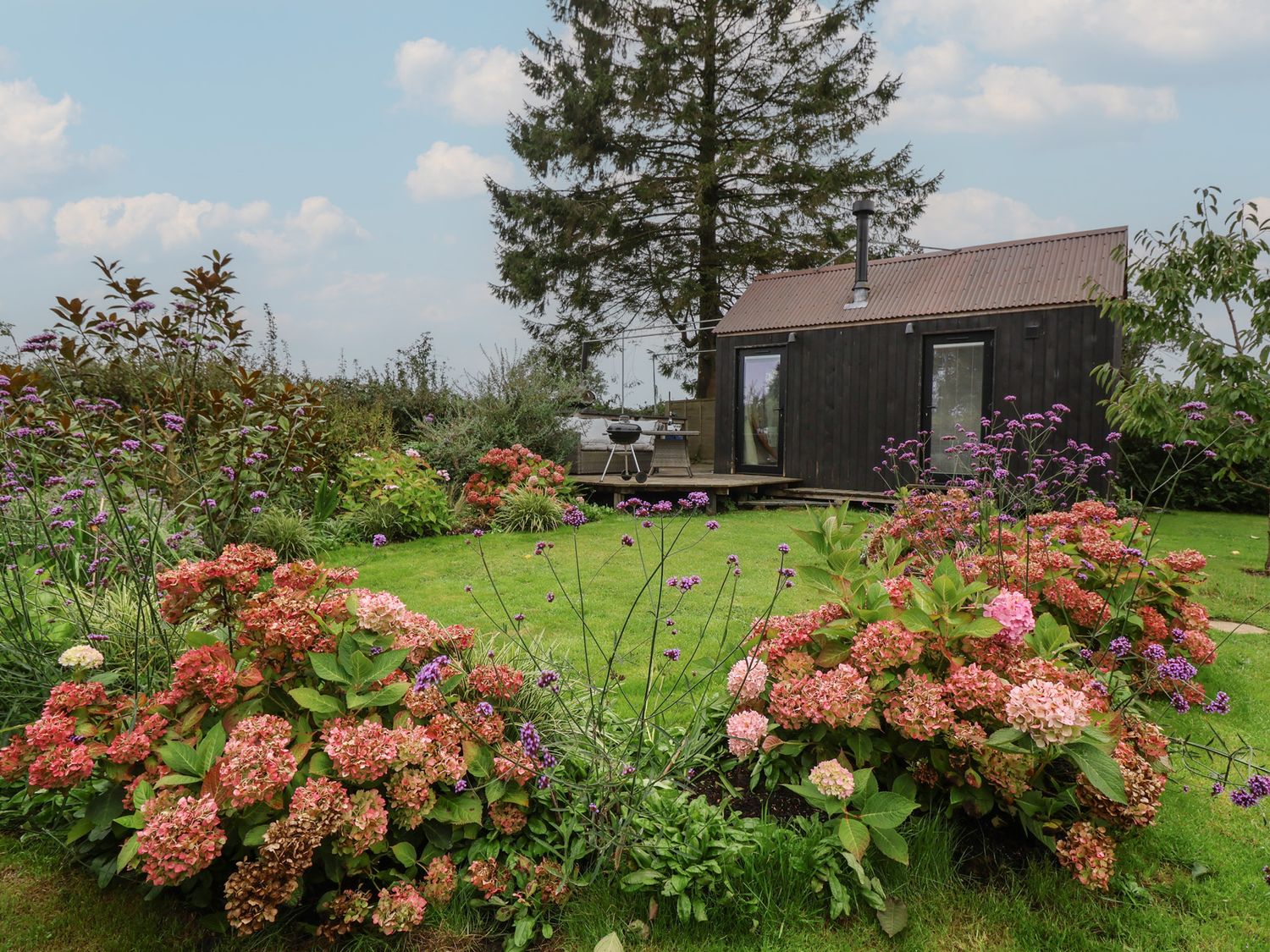 A garden with flowers and a house with a deck at The Bothy in 