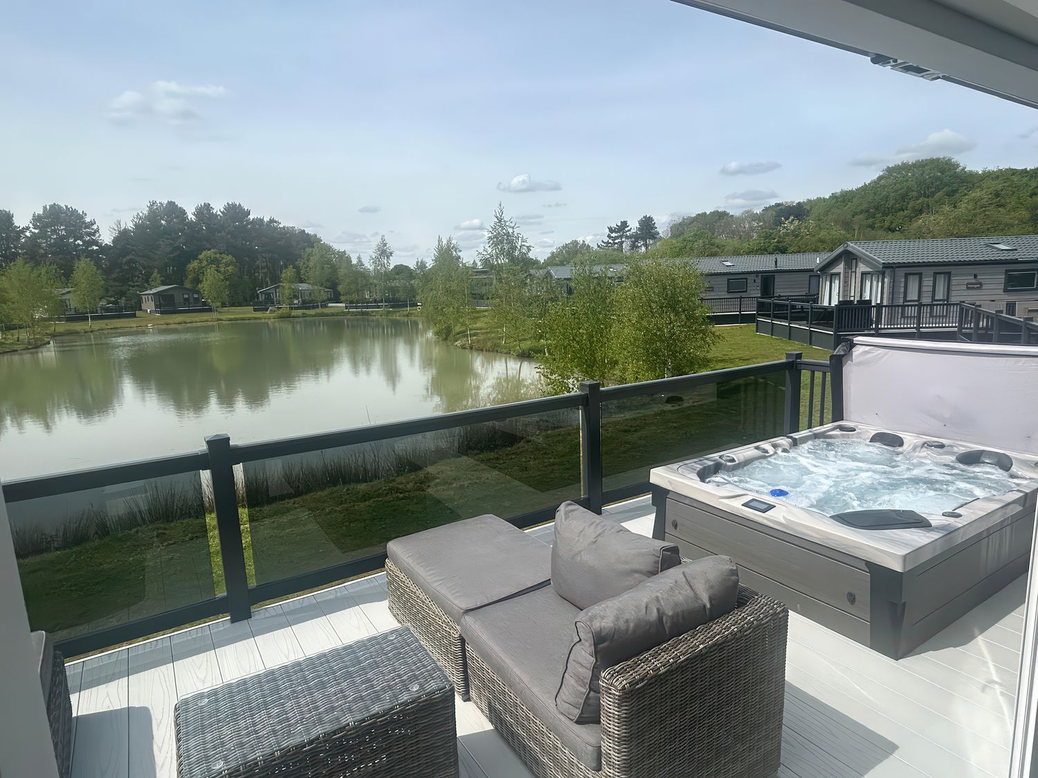 An outdoor area with a hot tub and sofa overlooking a lake at Hotchkin Lodge Woodhall Spa