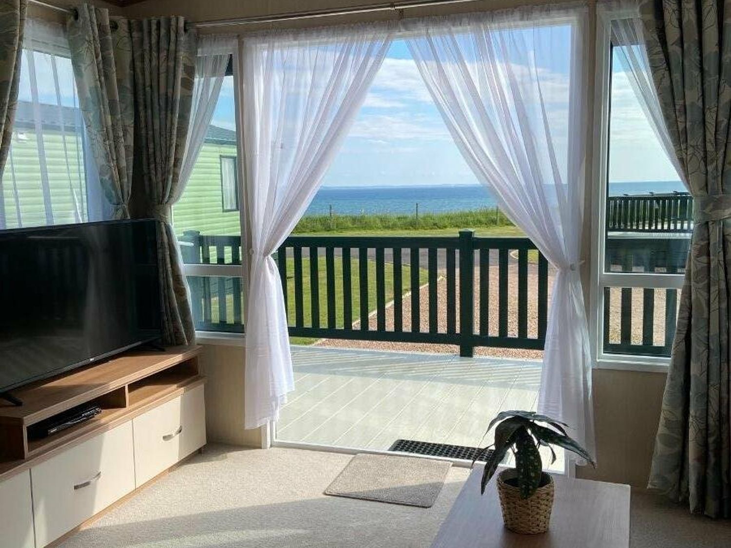 a living room with a TV and curtains overlooking a sea view at St Andrews Holiday Park - Holiday Accommodation 12987, St. Andrews