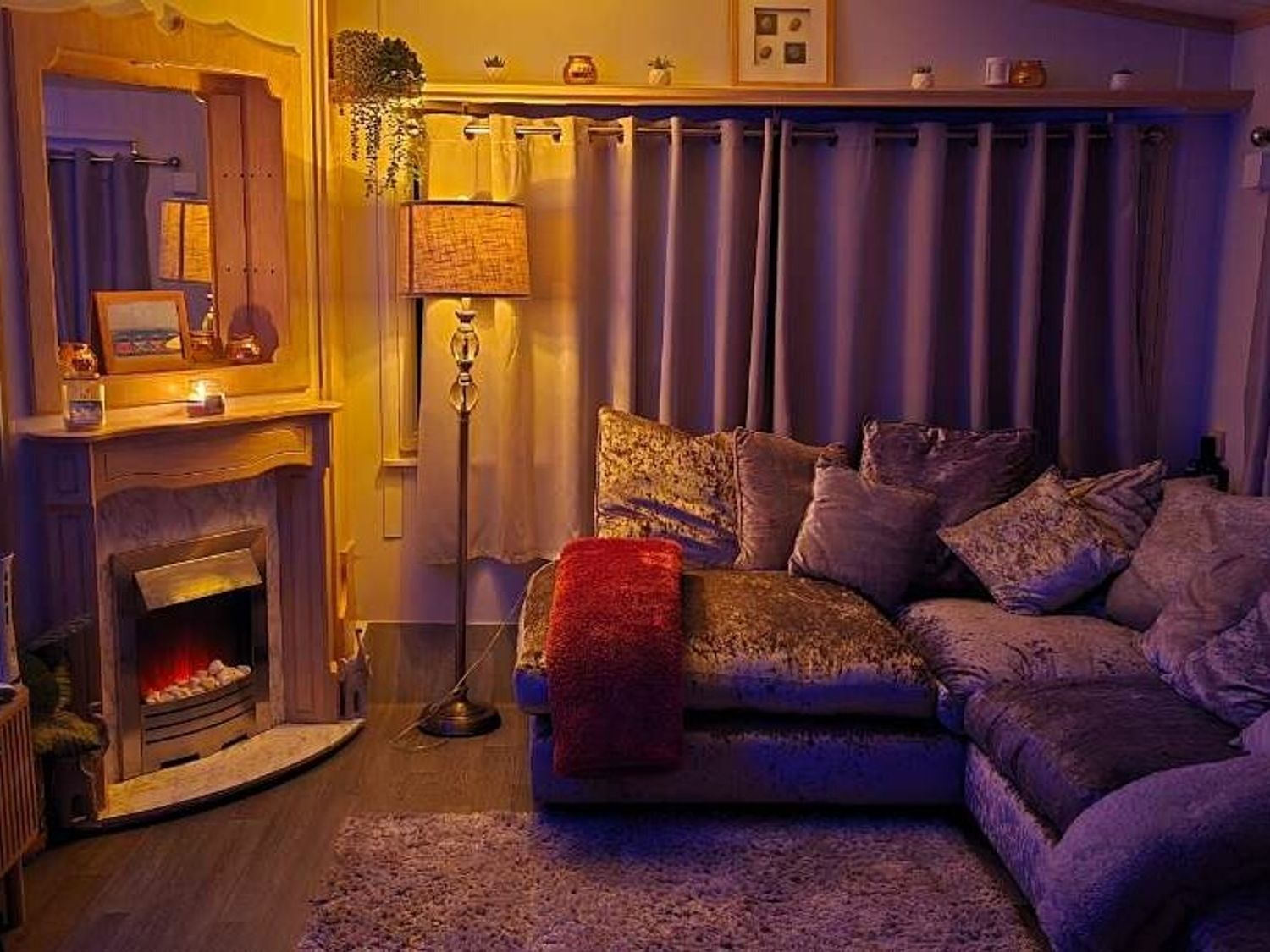 a cozy living room with a sectional sofa, floor lamp, and an electric fireplace at Hafan y Mor Haven - Holiday Accommodation 18358, Pwllheli