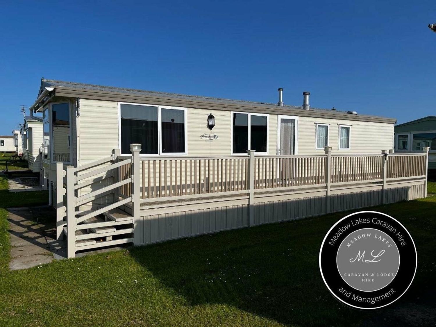 a caravan with a wooden deck and railings at Meadow Lakes Caravan Hire and Management in an outdoor setting