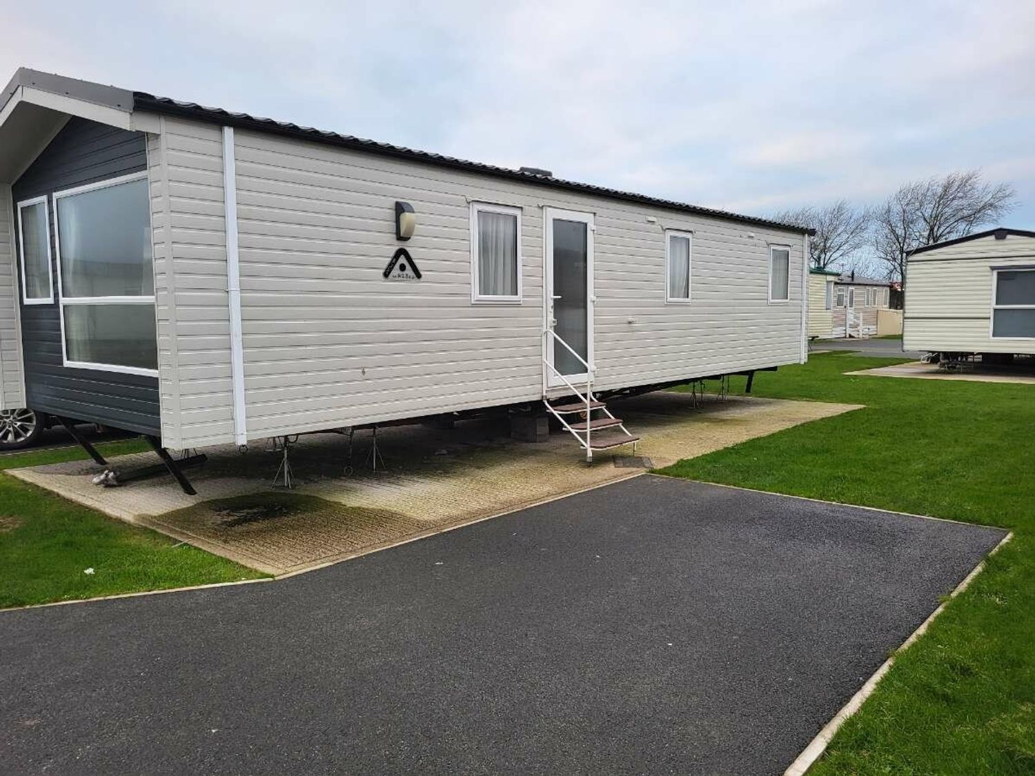 a mobile home parked on a concrete base with grass and pathways at Ty Mawr Holiday Park - Holiday Accommodation 21121 Ty Mawr