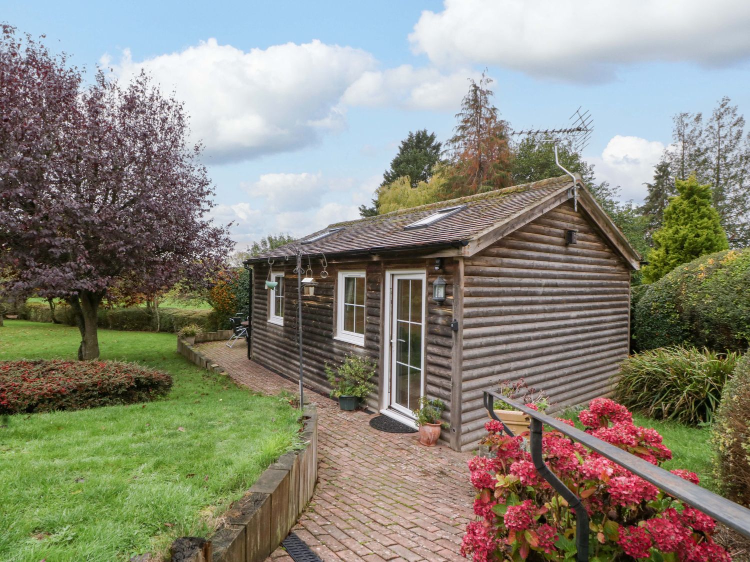 A wooden cabin in a garden with a pathway and flowers at The Log Cabin in Corse near Gloucester