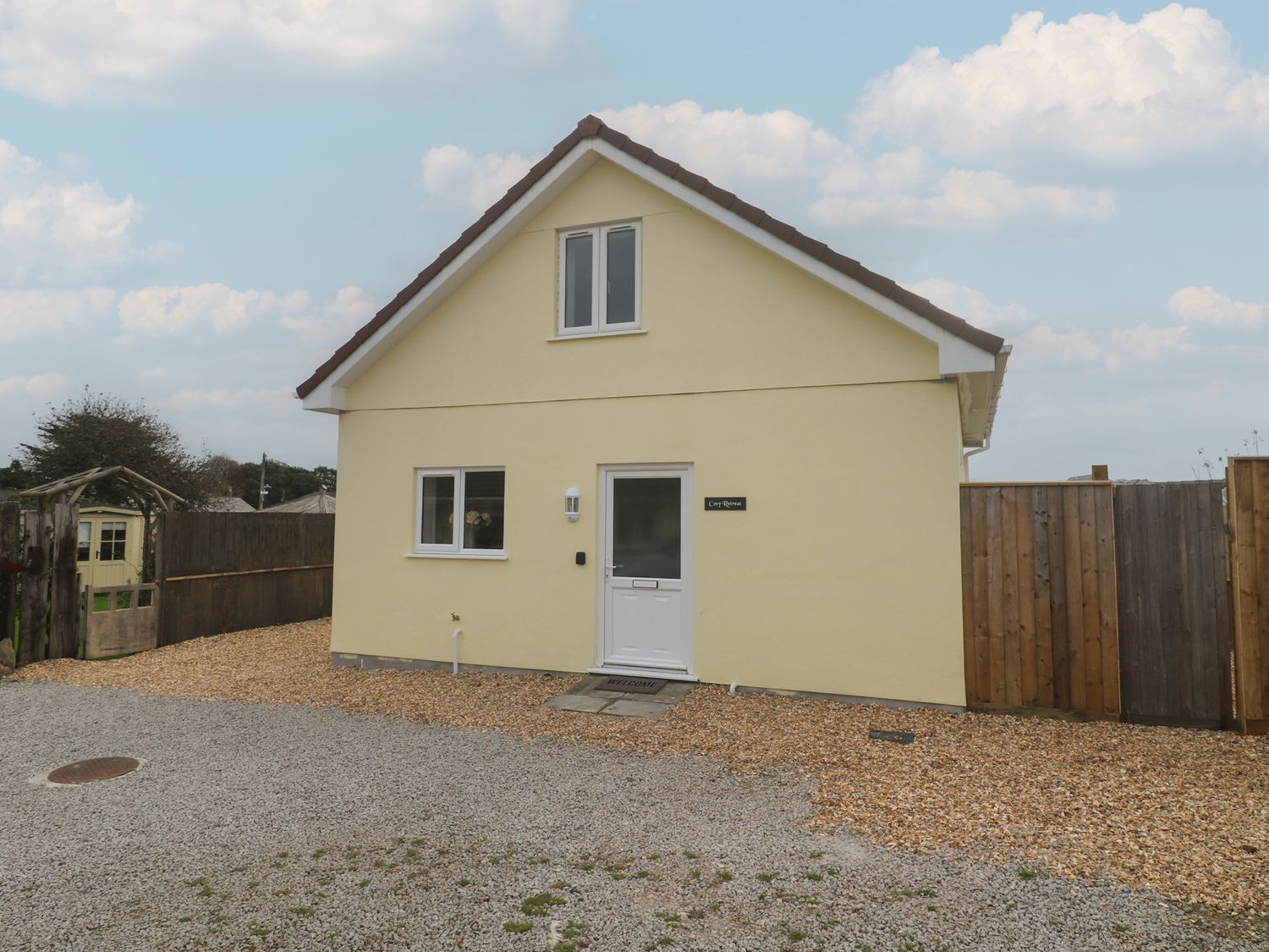 A house with a gravel driveway and a lawn at Cosy Retreat