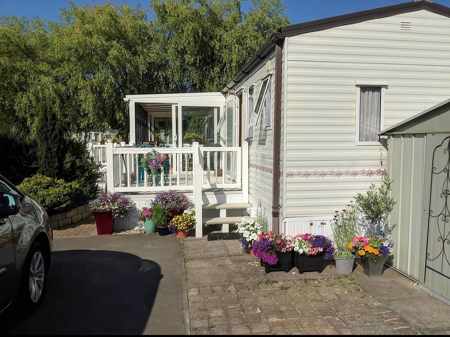 A mobile home with a deck and flowers in planters at a property