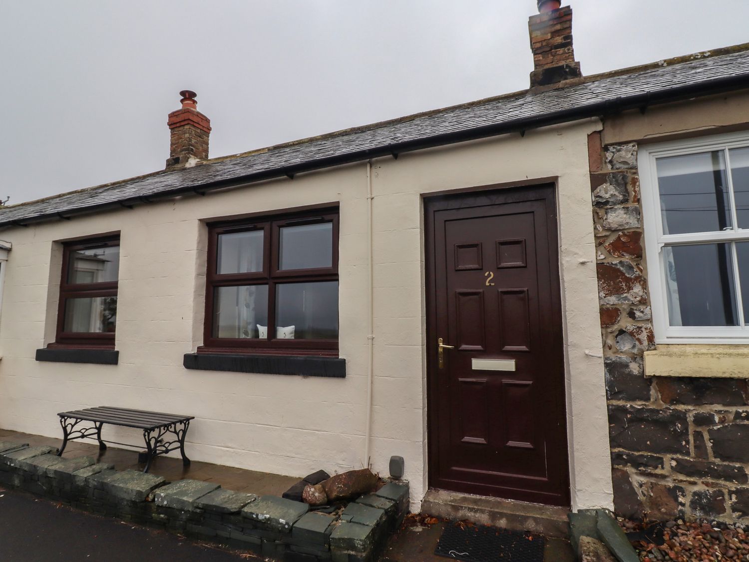 An outdoor view of a cottage with a bench and door at Sunny Brae in Alnwick