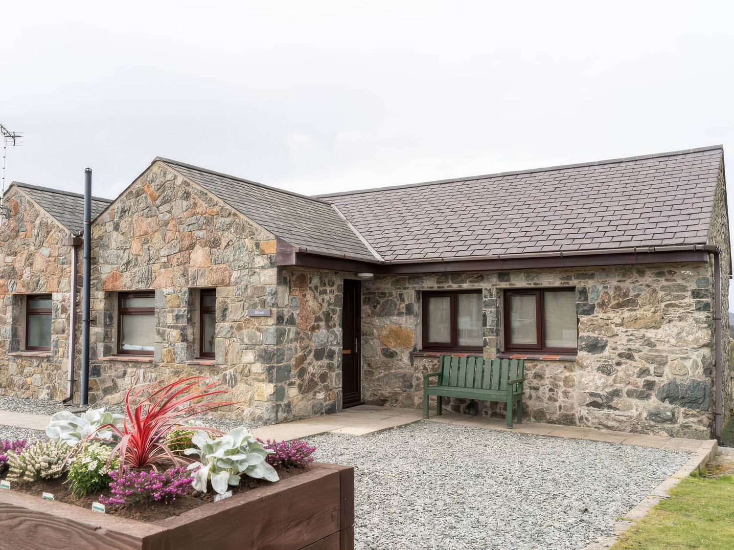 A stone house with a gravel area and bench at Wren Cottage in Llangaffo