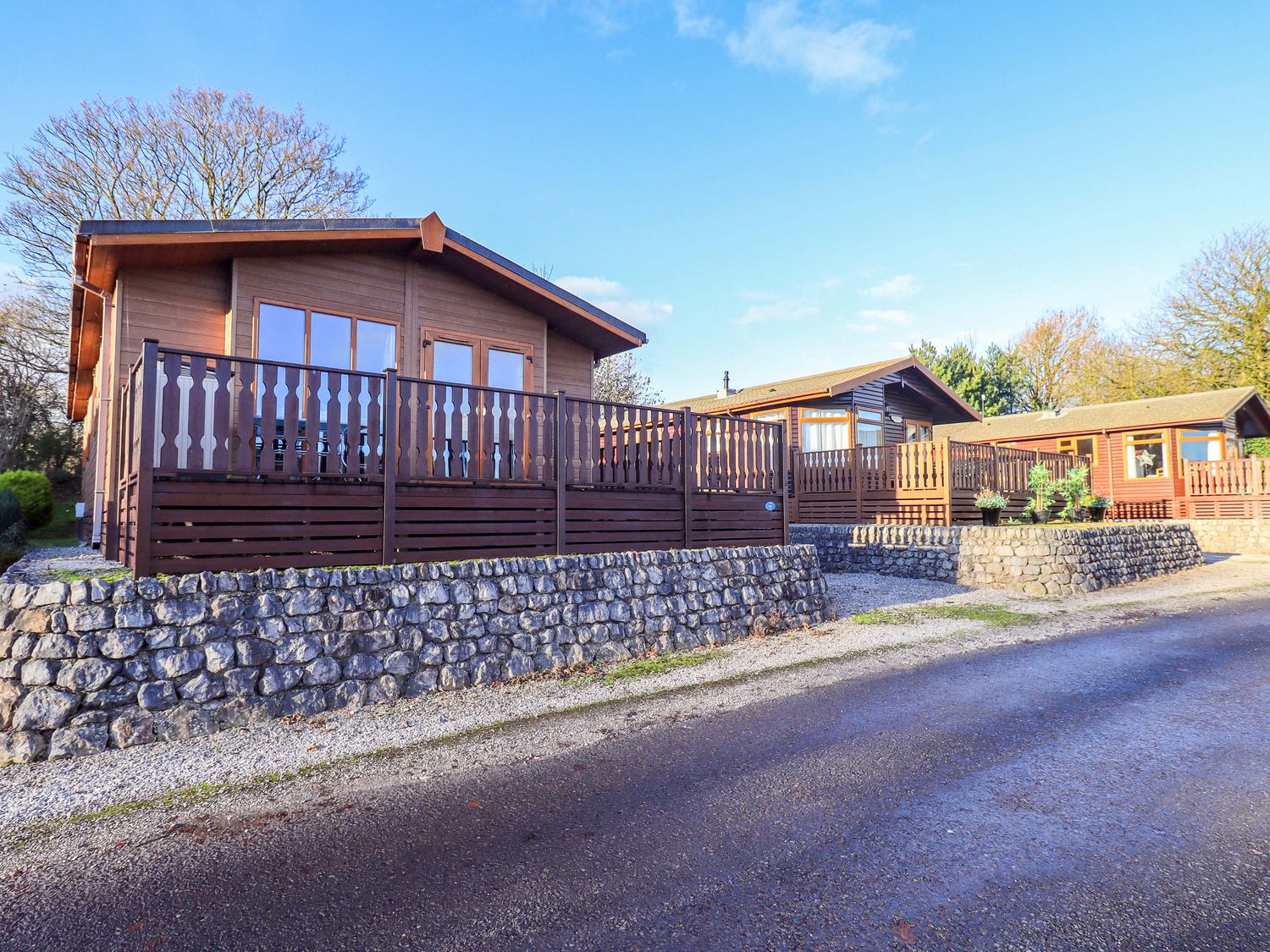 A log cabin with a deck and stone wall at Kingfisher Lodge 