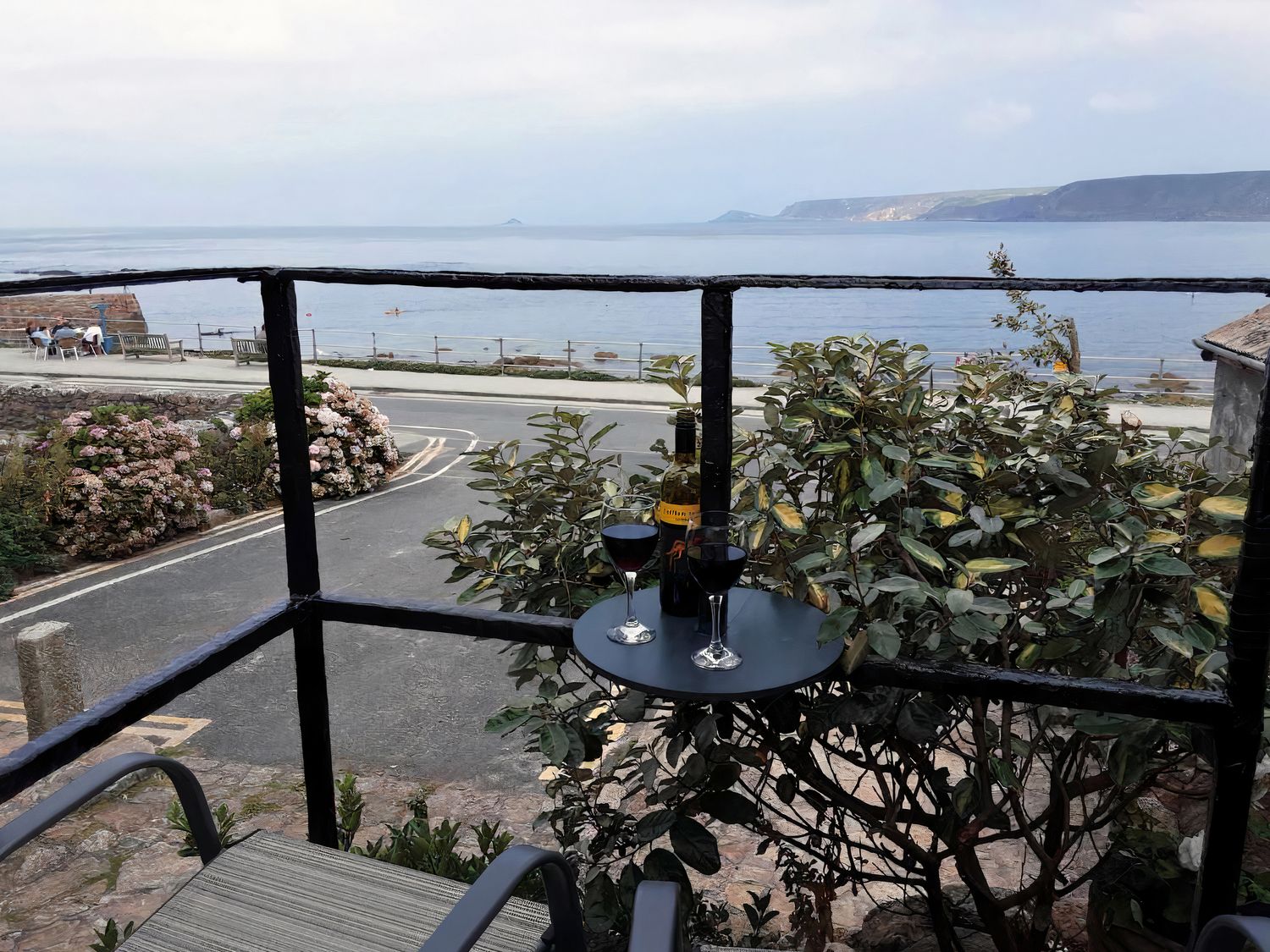 A balcony with wine glasses and a bottle overlooking the sea at Cove Retreat in Sennen Cove