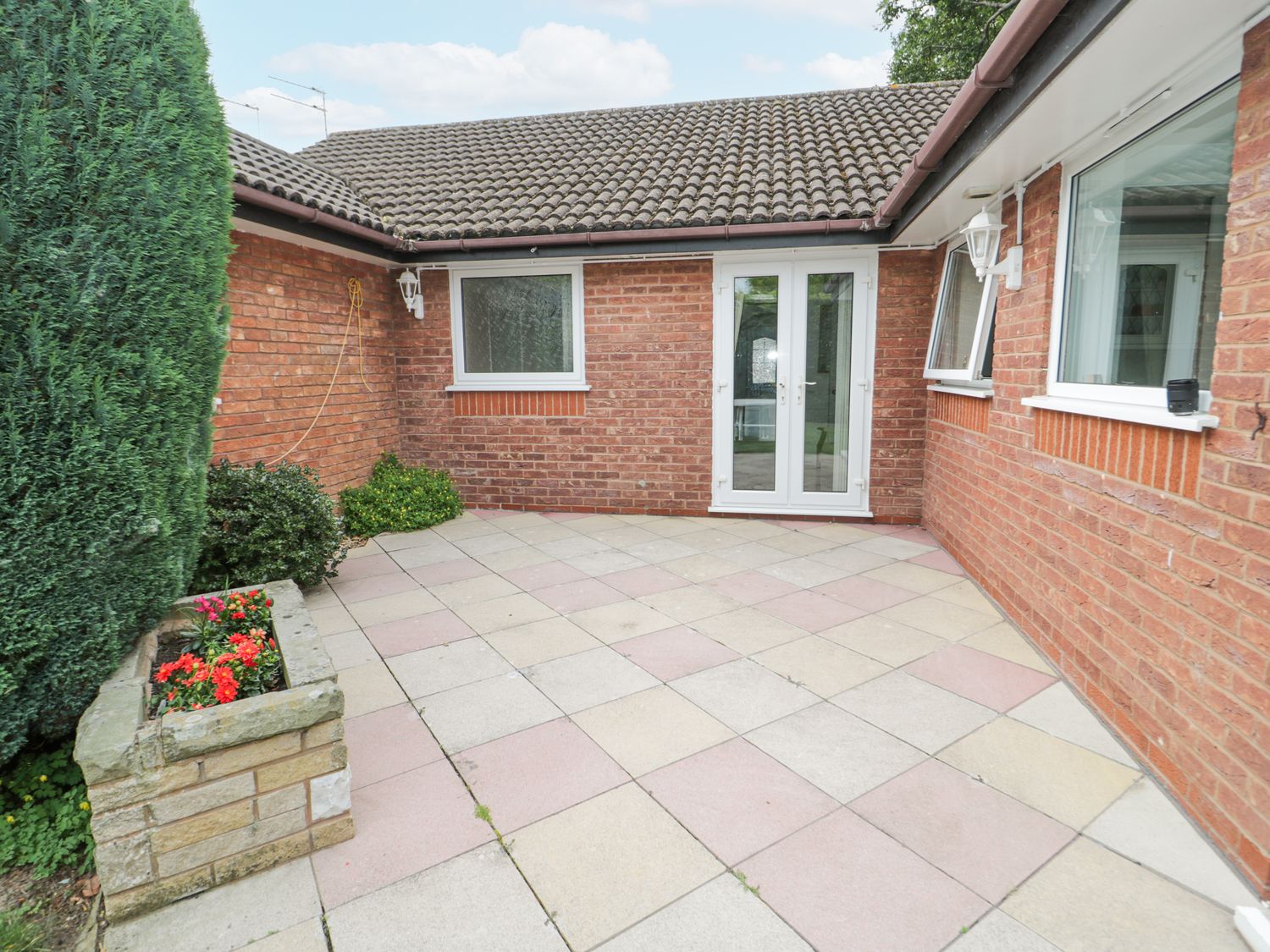 A tiled patio area with brick walls a flower planter and shrubbery at Breve Rest in Abergele