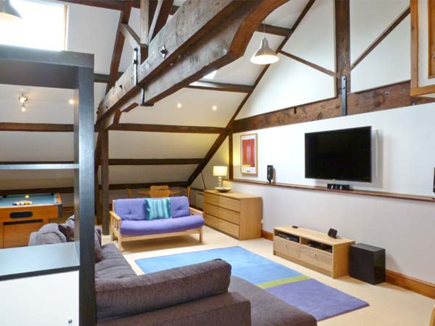A living room with wooden beams, two sofas, a rug, a wall-mounted TV, a wooden cabinet, and a pool table at Riverside Walk in Airton near Malham