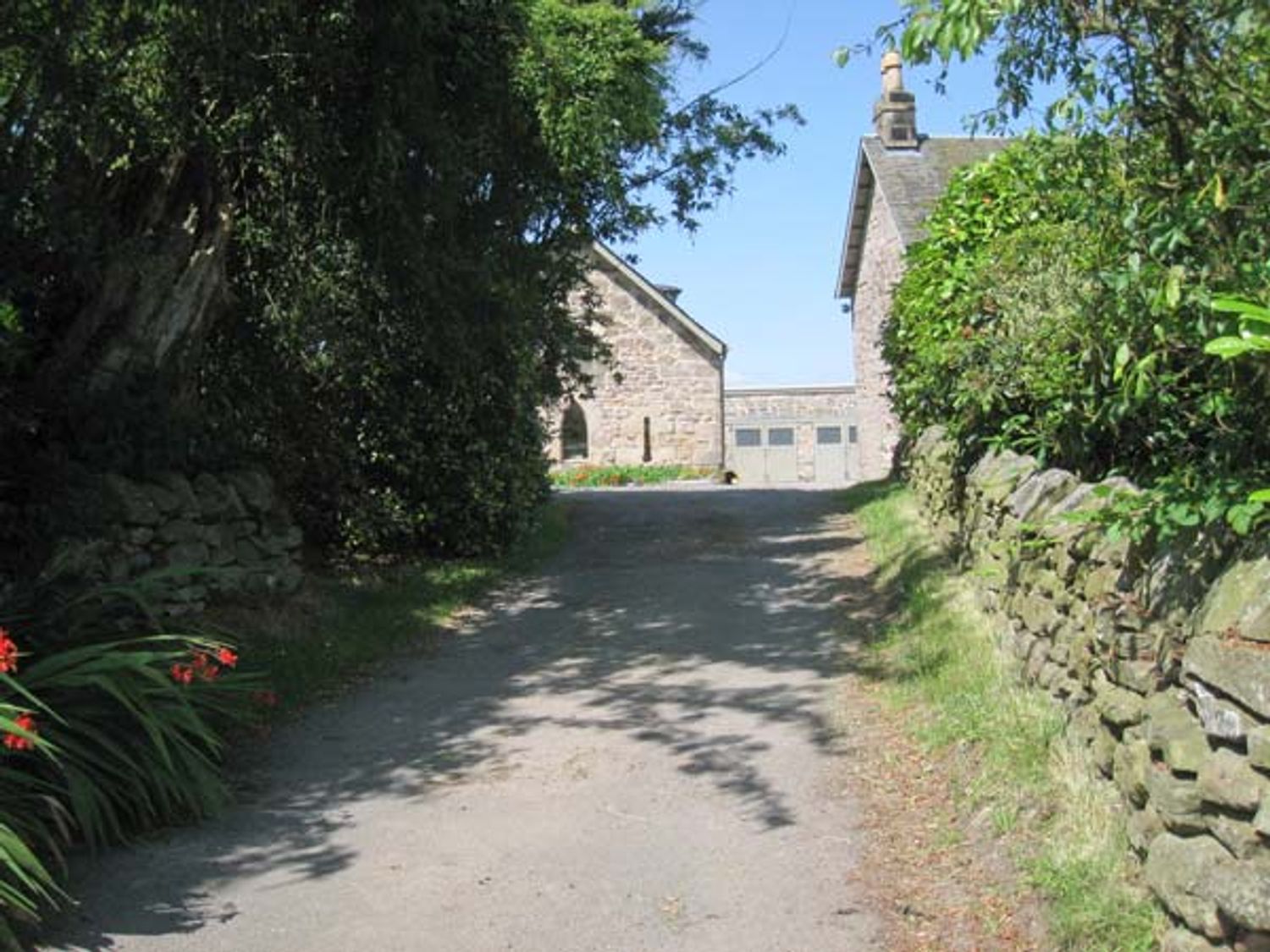 A stone driveway with stone walls and trees leading to stone buildings at Muirmailing Cottage in Plean near Stirling