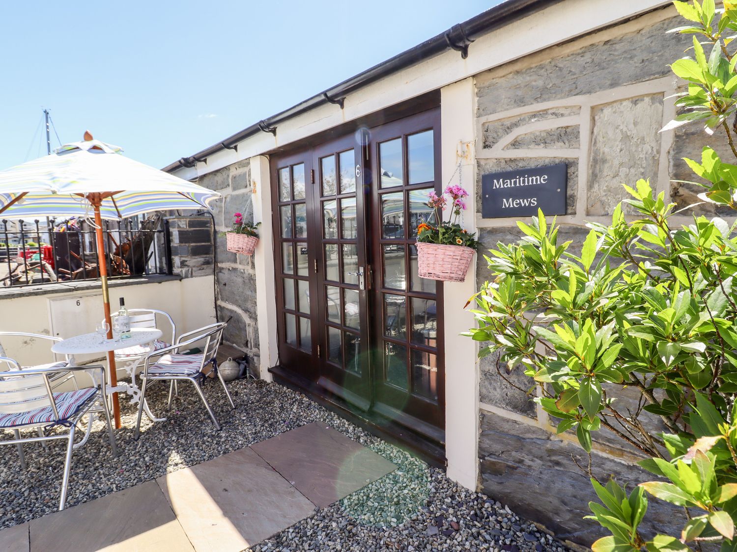 An outdoor seating area with a table umbrella and chairs outside a stone building with glass doors at Maritime Mews 6 The Oakleys in Porthmadog