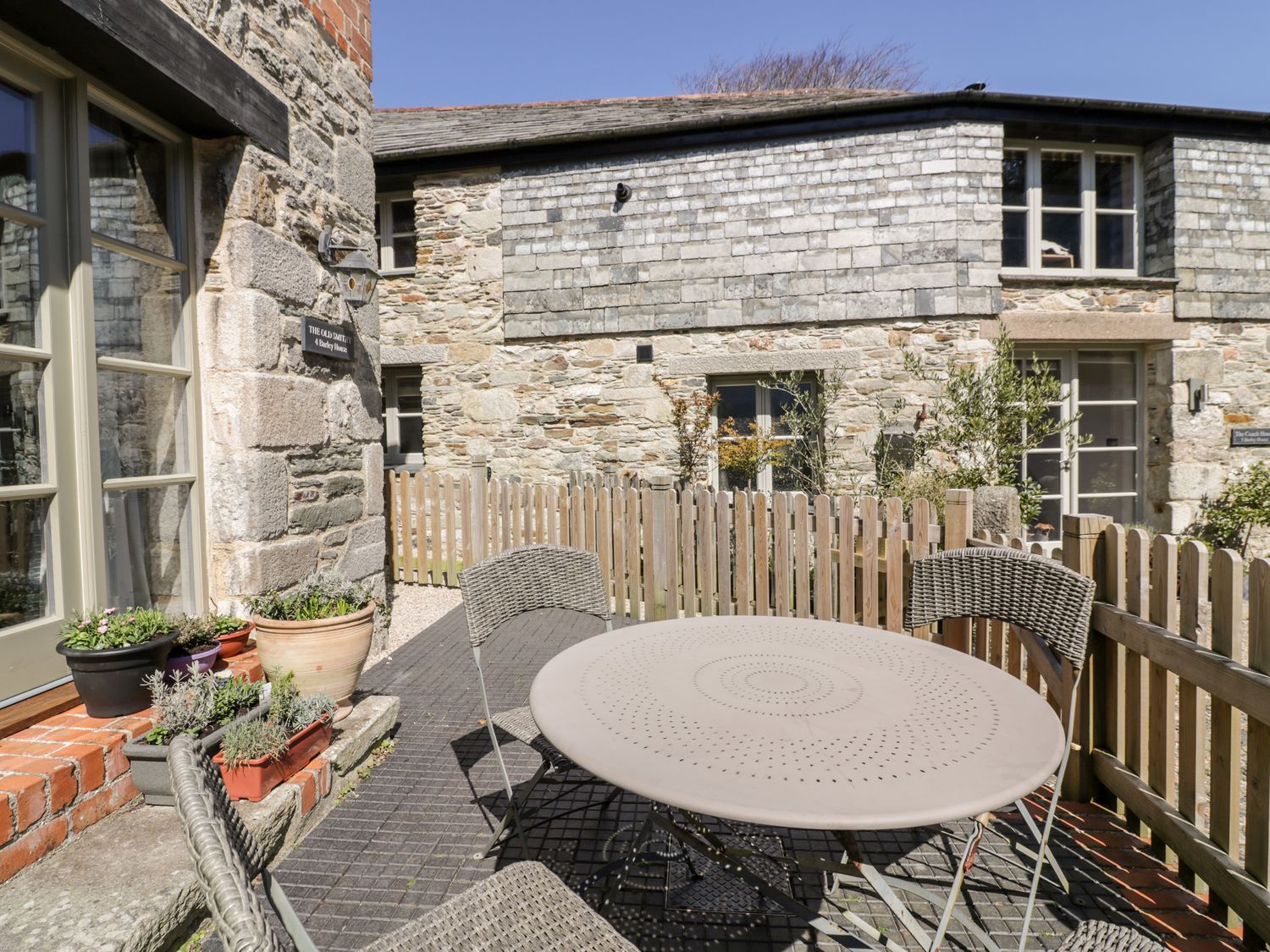 An outdoor patio area with a round table and four chairs beside a stone building with potted plants at The Old Smithy in St Columb Major near Newquay
