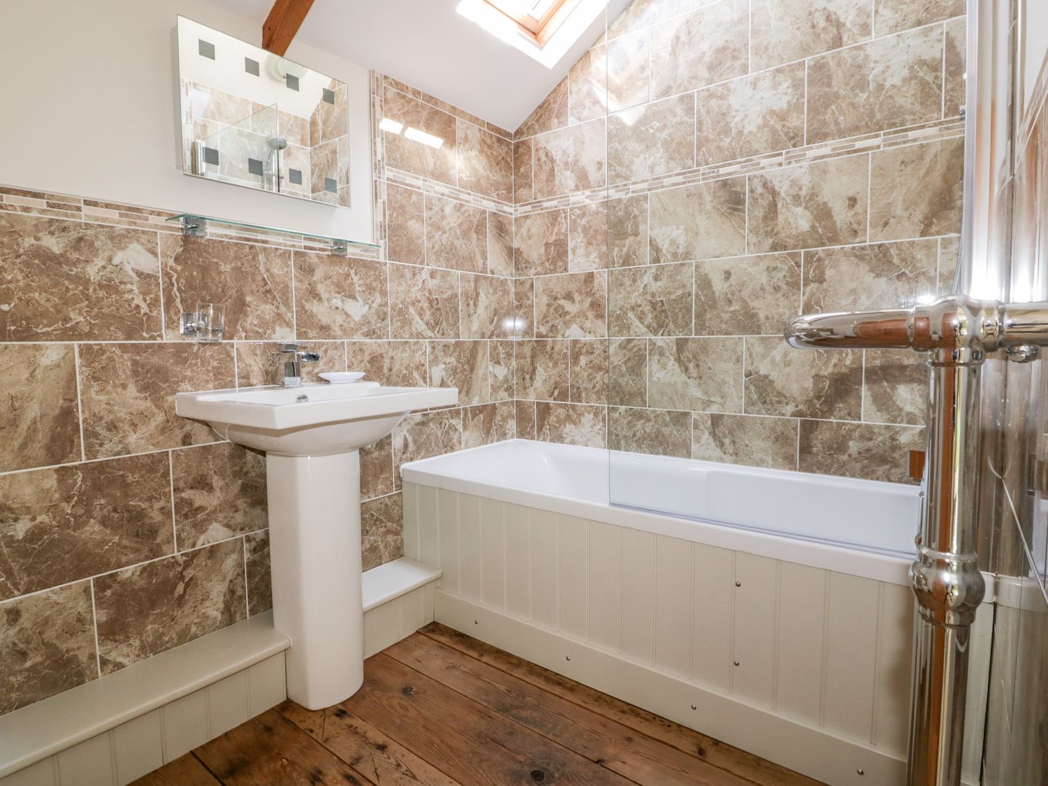 A bathroom with a pedestal sink bathtub with glass screen and tiled walls at The Old Smithy in St Columb Major near Newquay