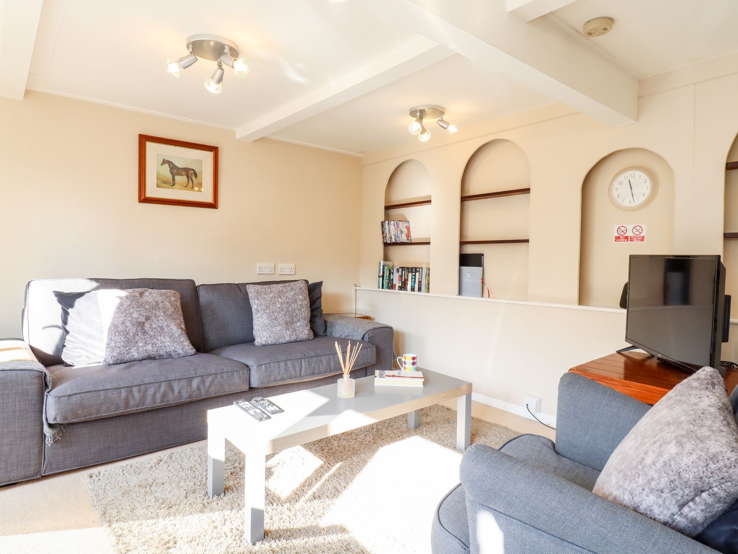 A living room with grey sofas a coffee table a television and shelves with books at Vine Cottage in Castle Hedingham