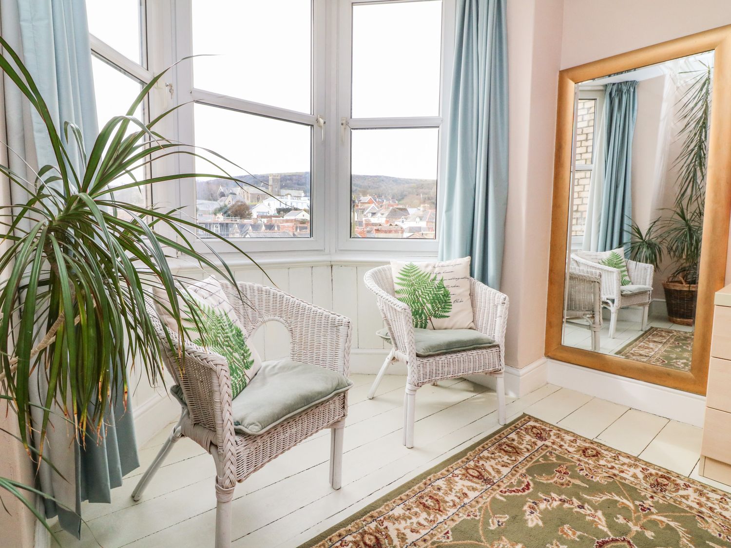 A room with two white wicker chairs with cushions near a large window and a tall mirror at Penryn in Ilfracombe