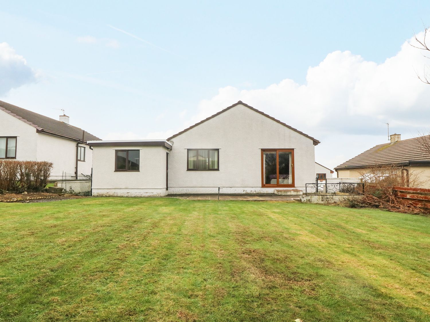 A backyard view of a single-story house with windows and a sliding door at Arwelfa Valley near Trearddur Bay